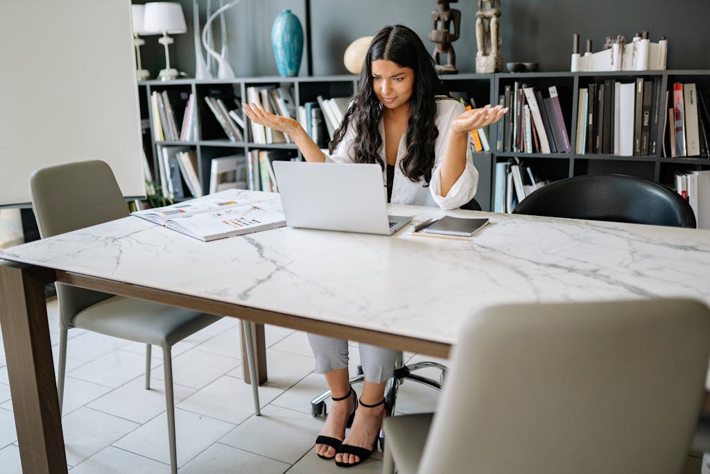 Woman sitting in an office with a laptop, working remotely with a confused expression.