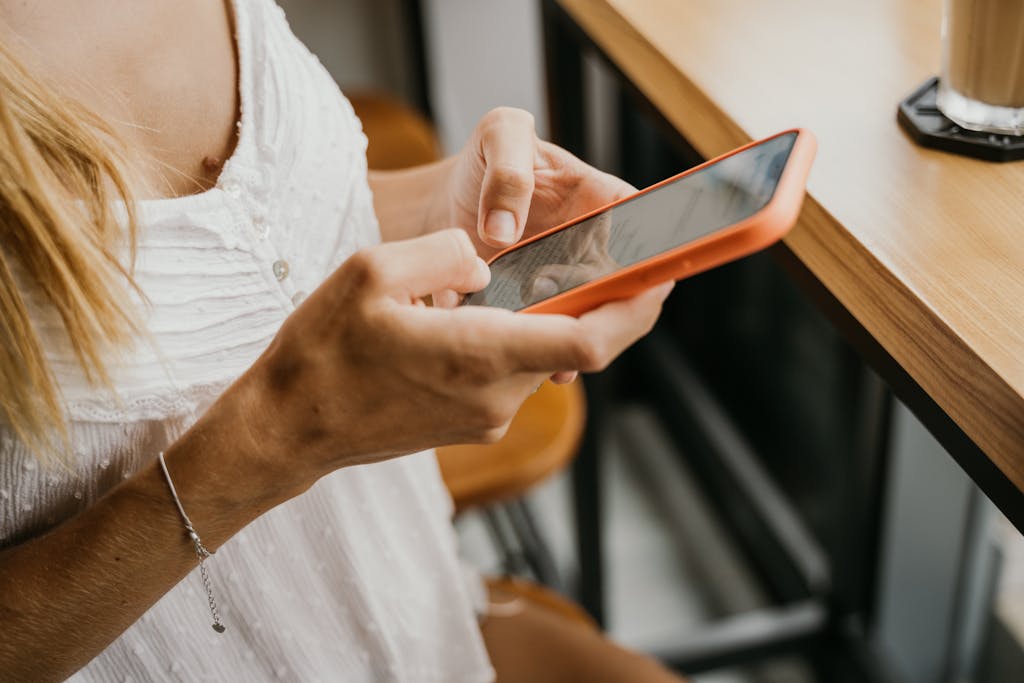 A woman using a smartphone at a wooden table in an indoor cafe setting.